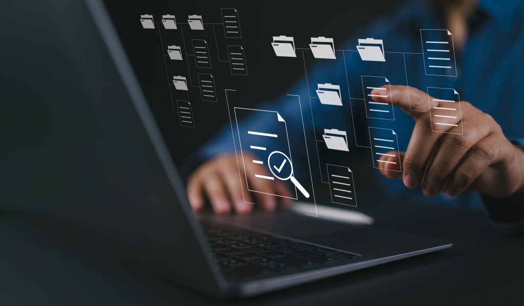 A closeup image of a person's hands using a laptop computer, and implying a database or archive interface visualized in the air in front of them.